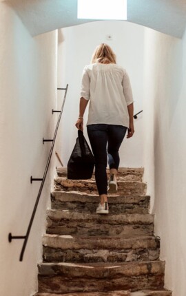 Eine Person steigt eine steinerne Treppe in einem hellen Stiegenhaus hinauf.