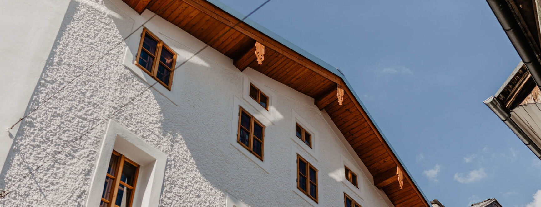 Mehrstöckiges Gebäude mit weißer Fassade und Holzdach, zahlreiche Fenster, blauer Himmel im Hintergrund.