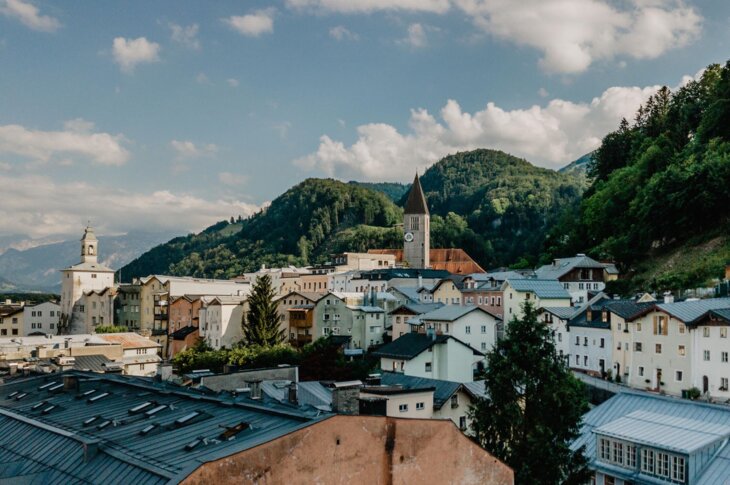 Stadtansicht von Hallein, umgeben von grünen Hügeln und einer Kirche mit Uhrturm im Zentrum unter blauem Himmel.