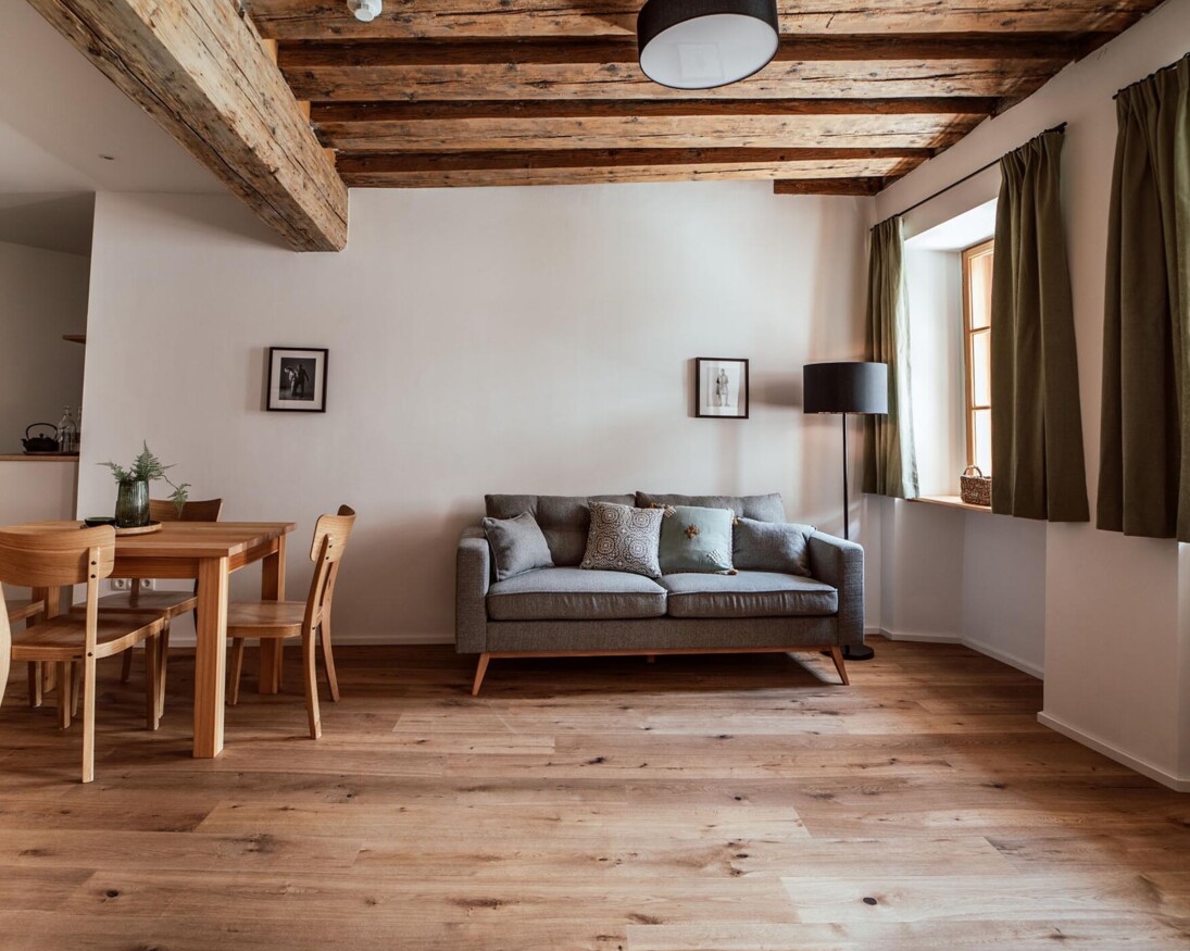 Wohnbereich mit Holzboden, grauem Sofa, Esstisch und einer voll ausgestatteten Küchenzeile. 