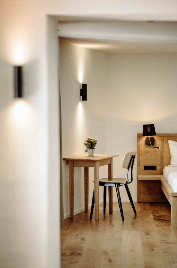 Gemütliches Zimmer mit Holztisch, Stuhl und Blumen, stilvoll beleuchtet.