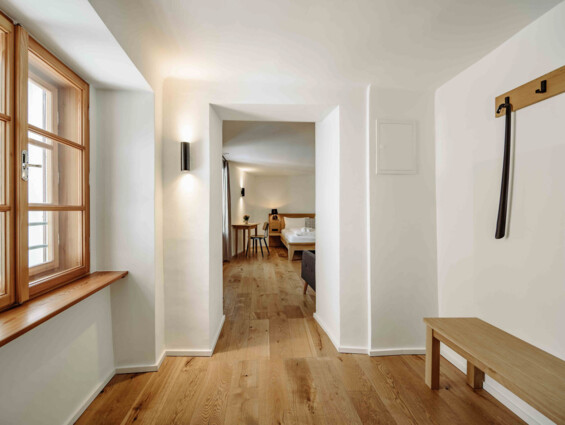 Heller Flur mit Holzboden, Fenster und Blick in ein gemütliches Zimmer im the salt Hallein.