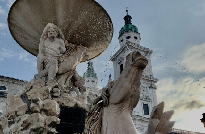 Brunnenstatue mit Pferdefigur am Salzburger Residenzplatz in der Dämmerung.
