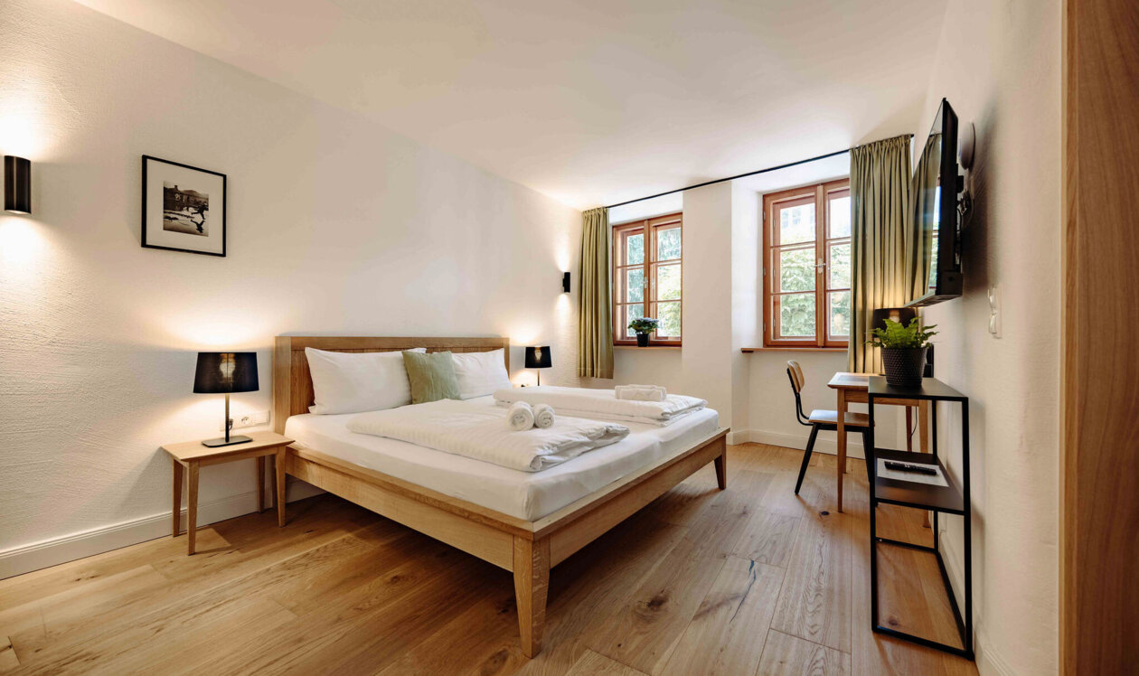 Gemütliches Schlafzimmer in stilvollem Apartment mit Doppelbett, Holzboden, TV und Schreibtisch.