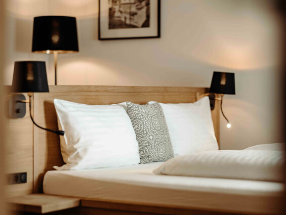 Hotelzimmer mit stilvollem Holzbett, dekorativen Kissen und modernen Lampen, das eine einladende Atmosphäre zum Entspannen bietet.